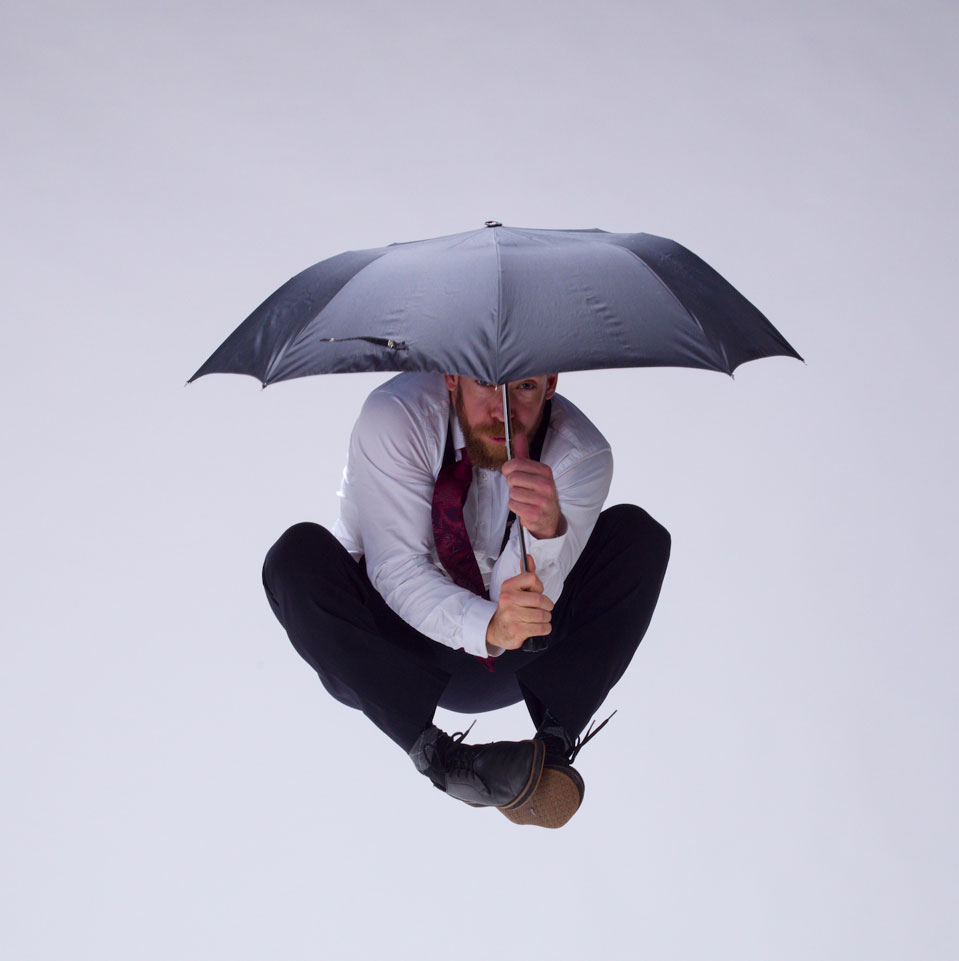 Dance artist Shay Kuebler jumps in the air while holding an umbrella