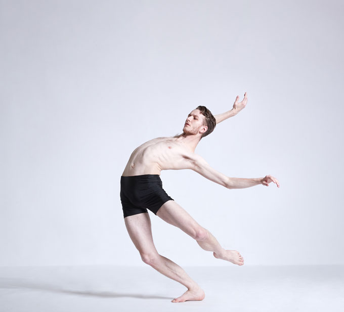 Male dance artist leans backwards with arms and one leg extended