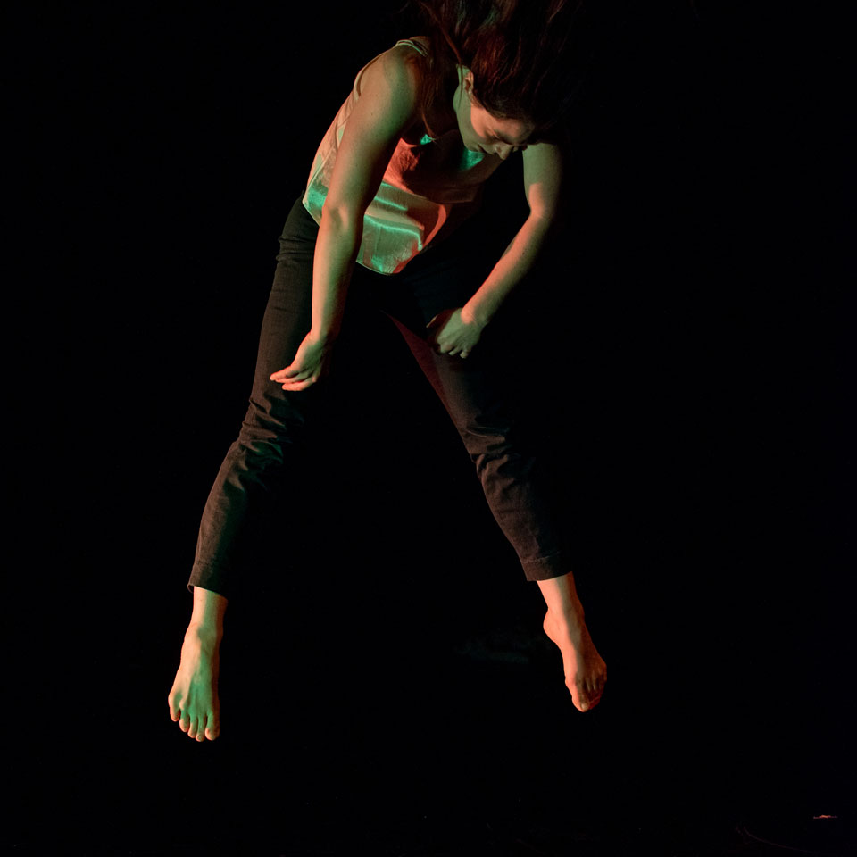 A female dance artist mid jump with her head bent over